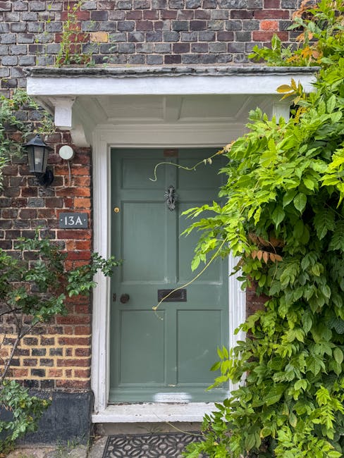 A close-up view of a residential front door painted in muted green, set within a brick house showing signs of weathering. Above the door, a white concrete or stone lintel forms an overhang. To the lef